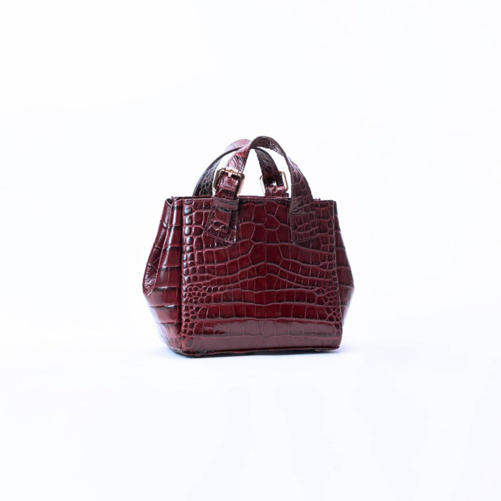 A small structured handbag with a glossy crocodile-embossed texture in deep burgundy, featuring dual top handles and a top zipper closure, set against a plain white background.