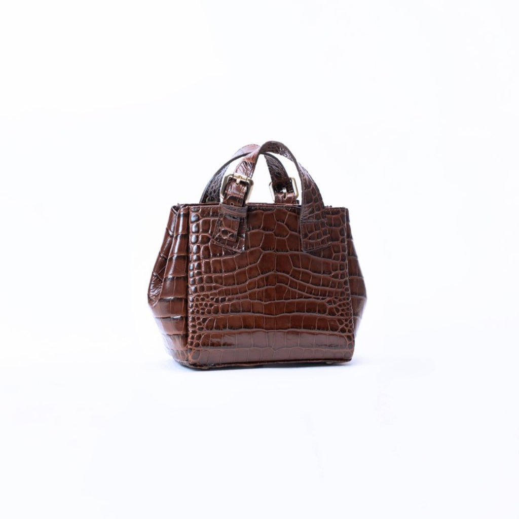 A small brown crocodile-embossed leather handbag with top handles, photographed against a plain white background.