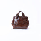 A small brown crocodile-embossed leather handbag with top handles, shown against a plain white background.