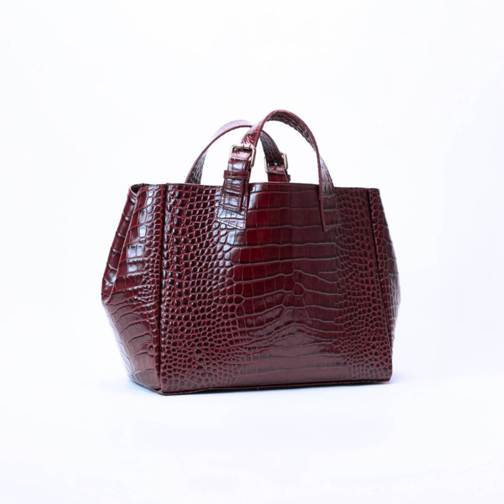 A dark burgundy crocodile-embossed leather handbag with top handles, photographed against a seamless white studio background.