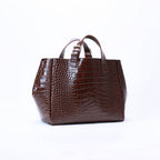 A dark brown crocodile-embossed leather handbag with dual top handles, photographed against a seamless white studio background.