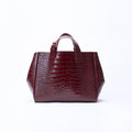 A structured handbag with a glossy crocodile-embossed texture in deep burgundy, featuring two top handles, set against a plain white background.