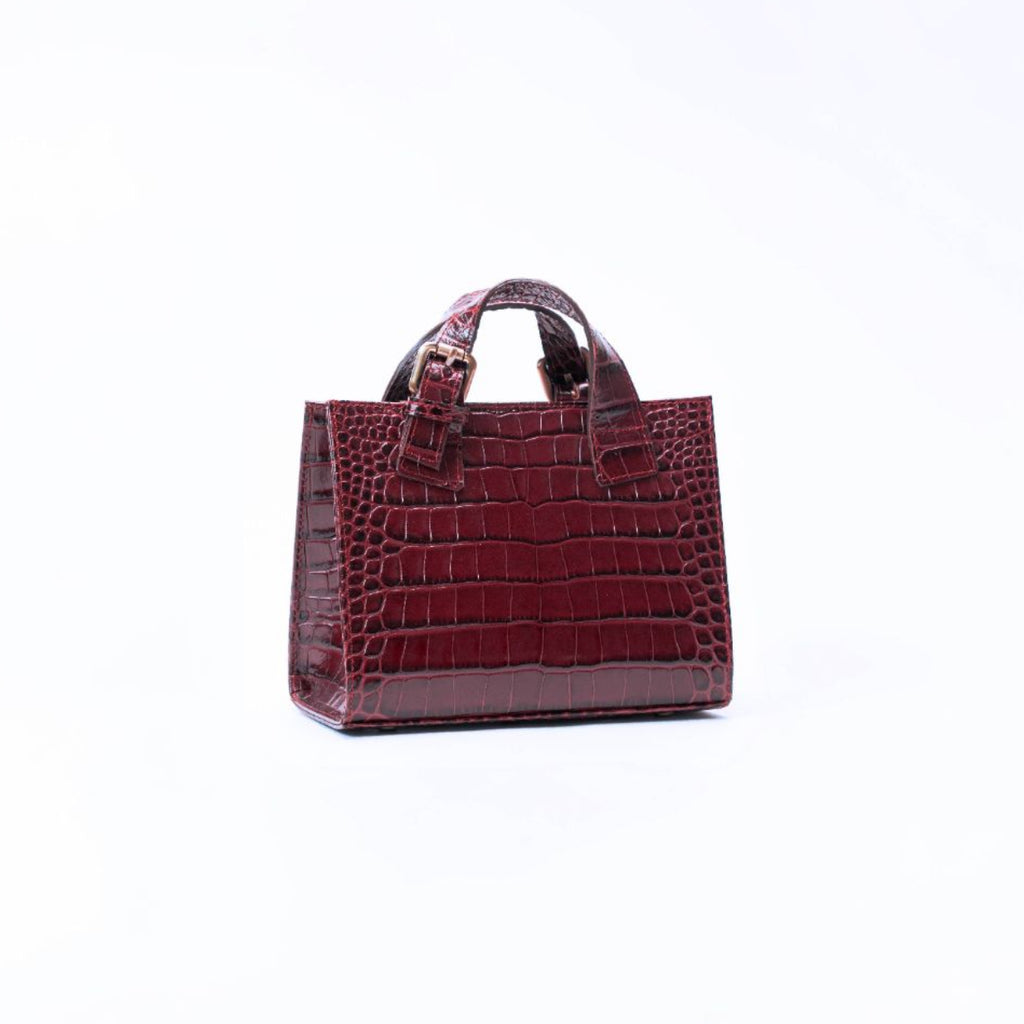 A small brown crocodile-embossed leather handbag with top handles, shown from the side against a plain white background.