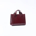 A small brown crocodile-embossed leather handbag with top handles, shown from the side against a plain white background.