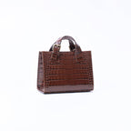 A small brown crocodile-embossed leather handbag with top handles, shown from the side against a plain white background.